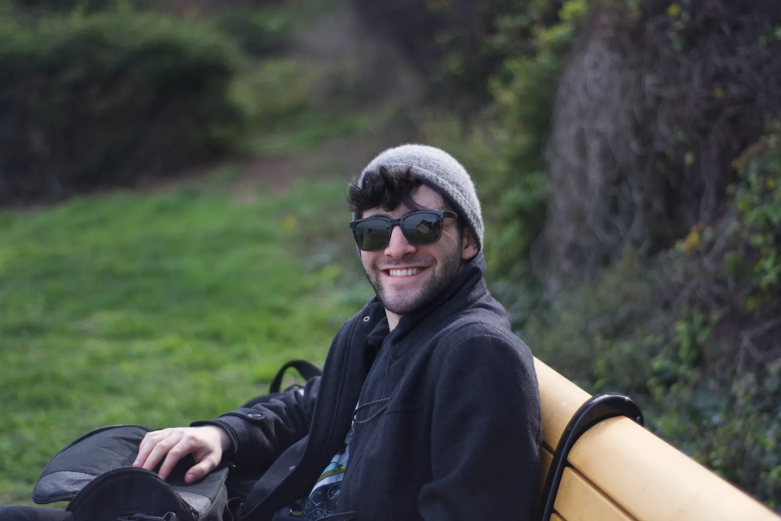 Sasha Novack smiling on a park bench, wearing sunglasses and a grey beanie