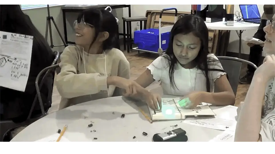 Students lighting up the circuit in a Rock, Paper, Physics! booklet during a class activity